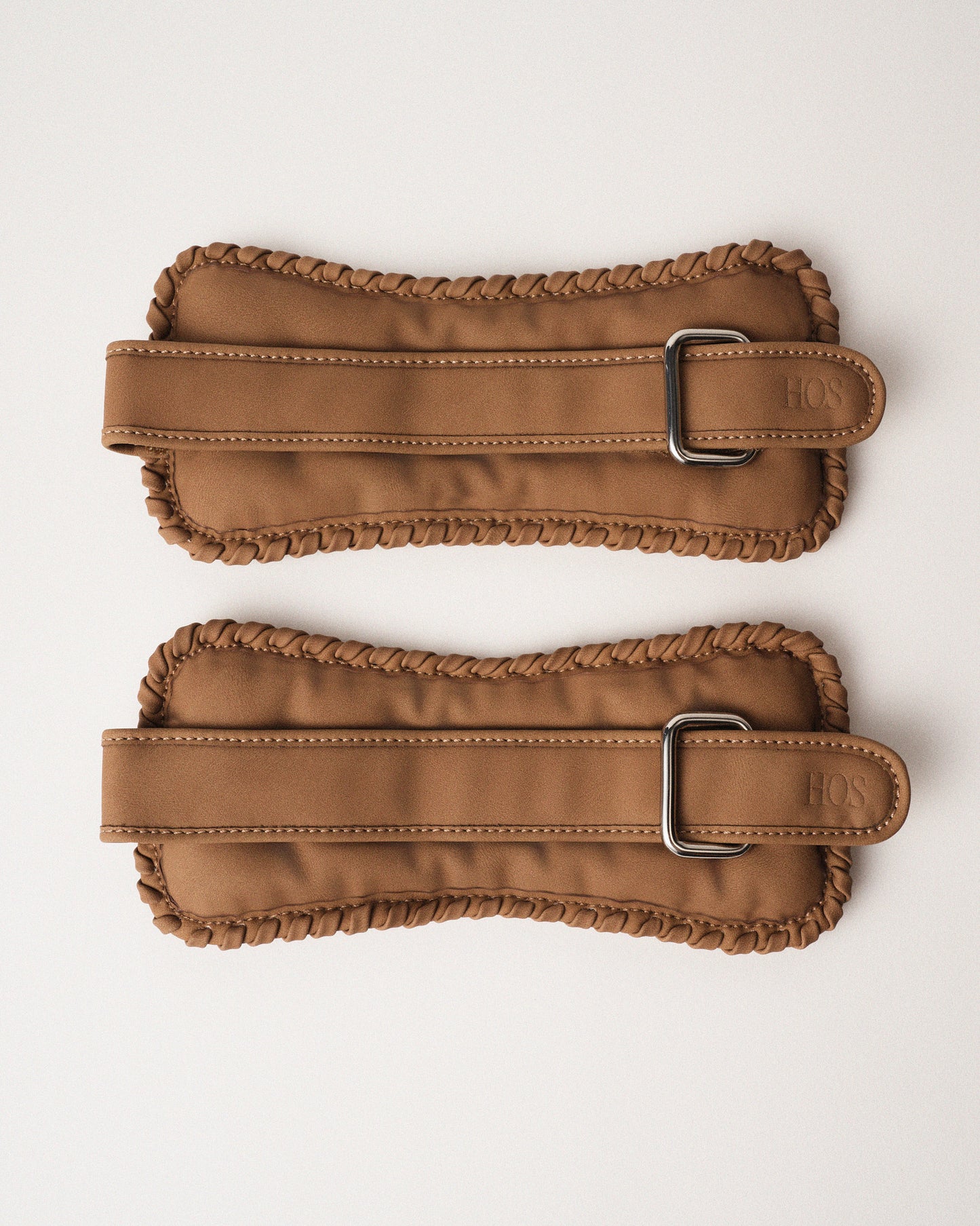 Two sand color ankle weights with our detailed signature stitch on the edges and metal buckles on a white background