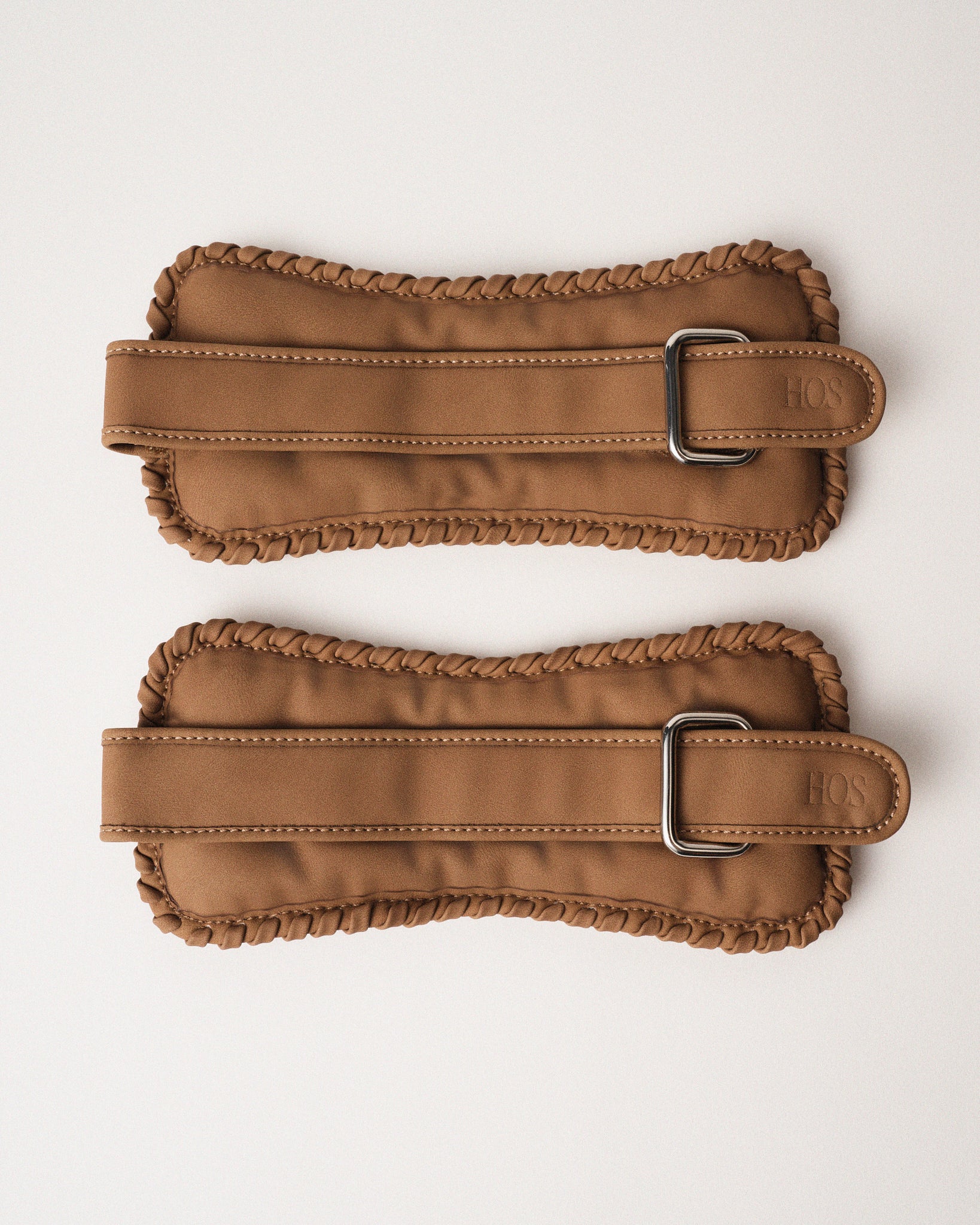 Two sand color ankle weights with our detailed signature stitch on the edges and metal buckles on a white background