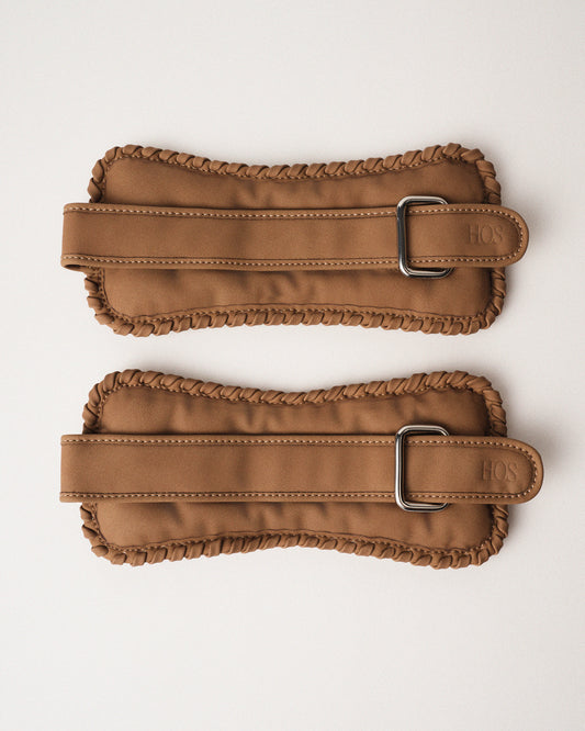 Two sand color ankle weights with our detailed signature stitch on the edges and metal buckles on a white background